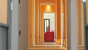 A long, narrow hotel corridor with a red seating area at the end. - Blurooms (Sorrento)