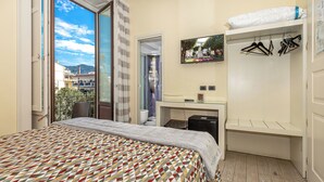 A bedroom with a patterned bedspread, a desk with a computer, a wardrobe, and a view of the outside. - Blurooms (Sorrento)