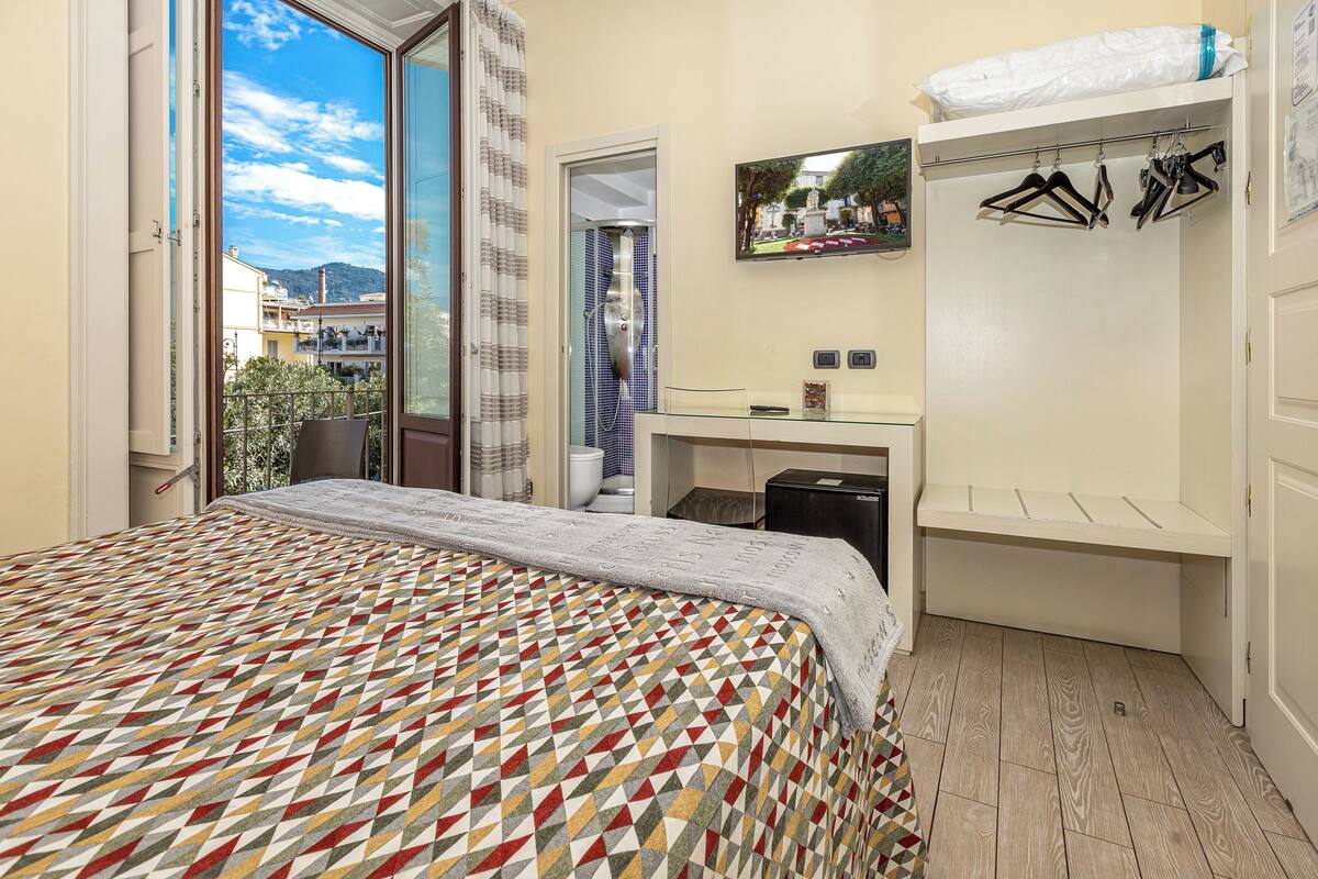 Un dormitorio con una colcha estampada, un escritorio con una computadora, un armario y vistas al exterior.