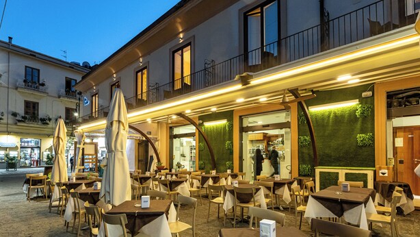 An outdoor cafe with tables and chairs, a green wall, and a balcony with railings. - Blurooms (Sorrento)
