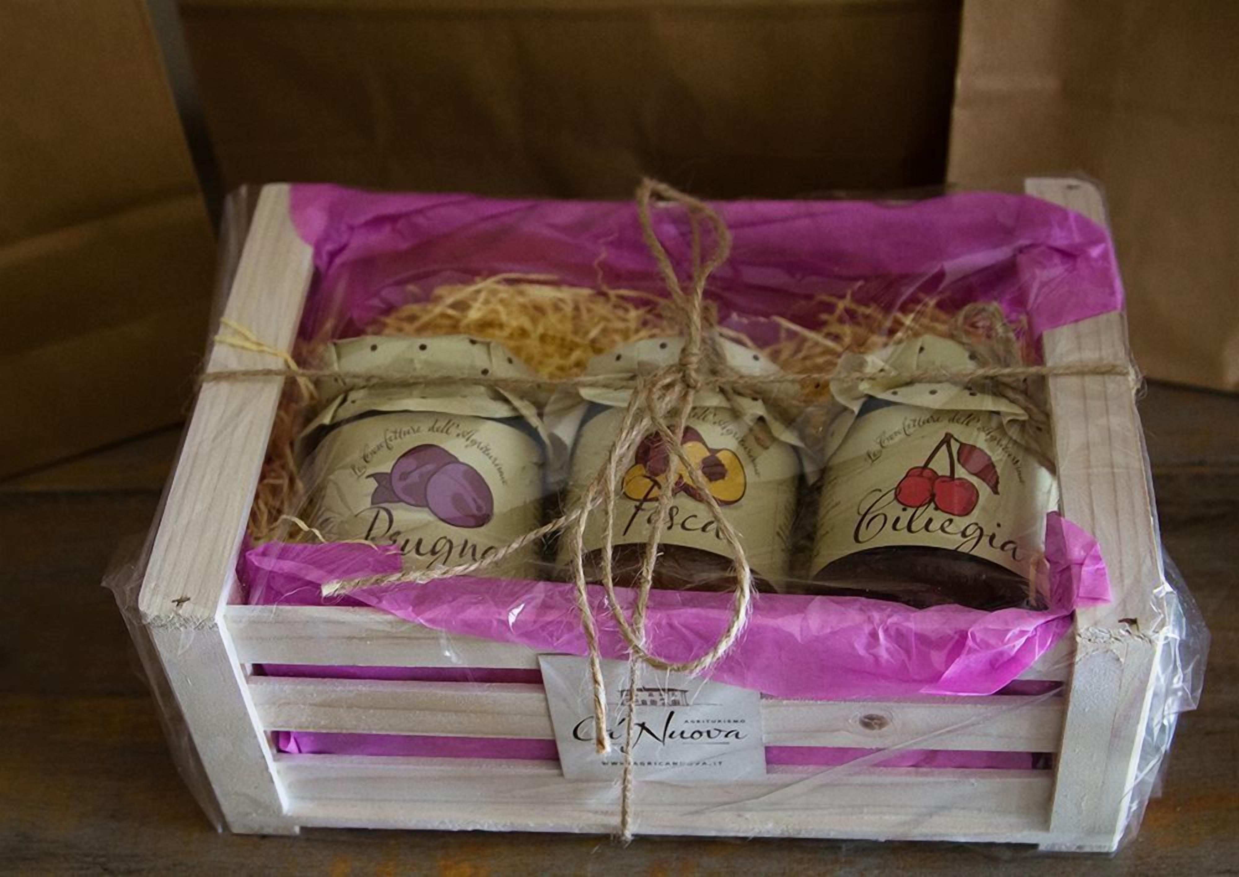 Une caisse en bois remplie de pots de fruits confits, ficelés avec de la ficelle et enveloppés de papier violet.