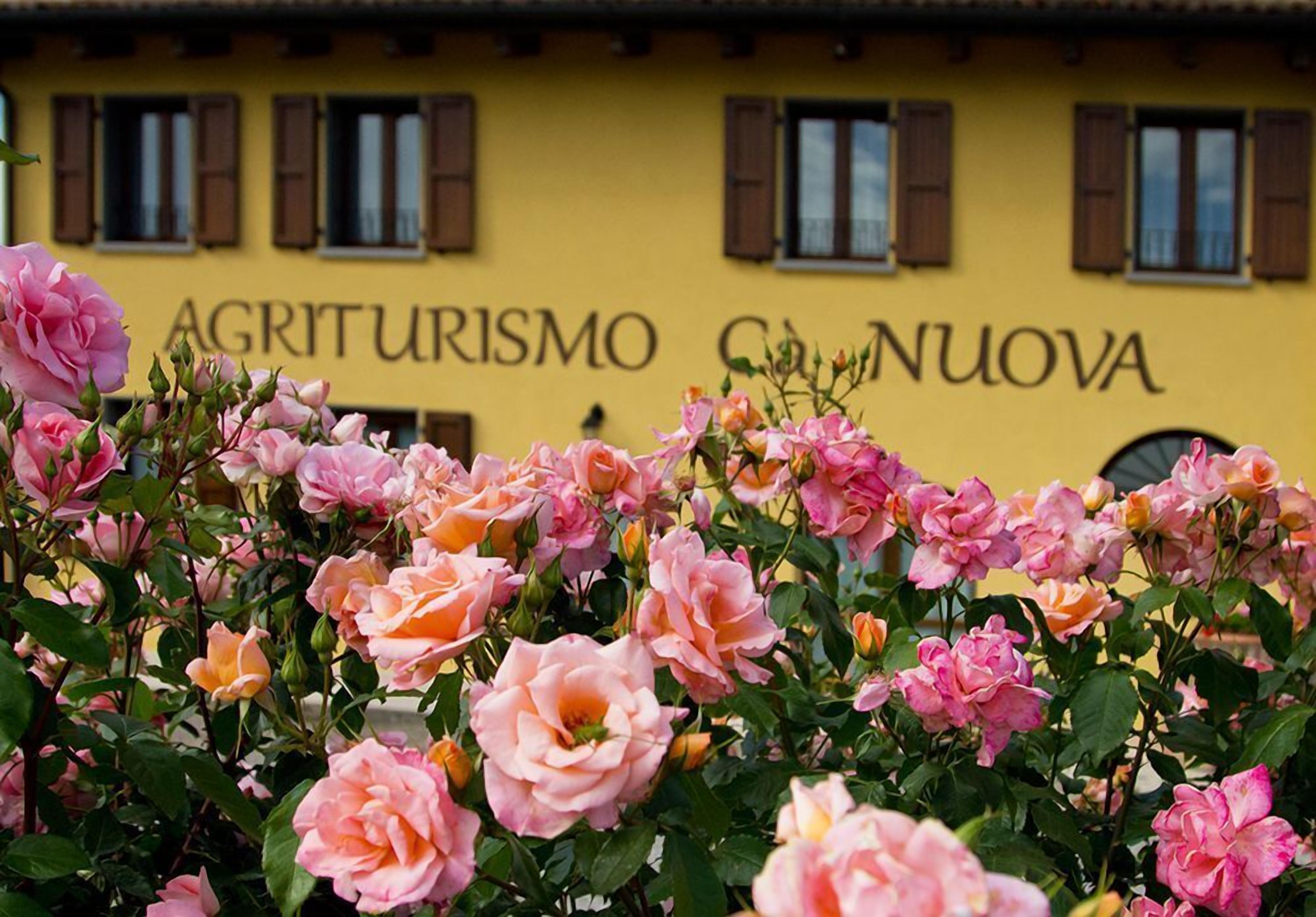 Un bâtiment jaune sur lequel on peut lire l’inscription « AGRITURISMO C’NUOVA », avec un jardin de roses roses devant.