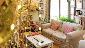 Una sala de estar acogedora con un sofá color beige, una pequeña mesa de centro blanca y una estantería llena de libros y juguetes.
