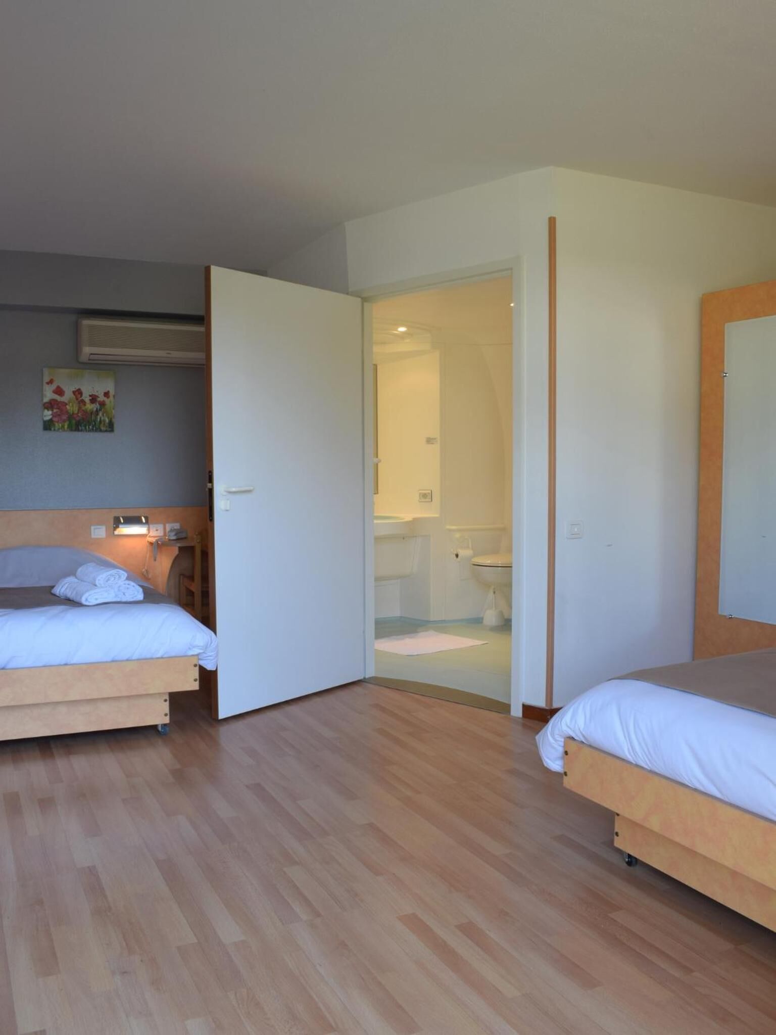 Een hotelkamer met twee bedden, een badkamer zichtbaar door een geopende deur, en een schilderij aan de muur.