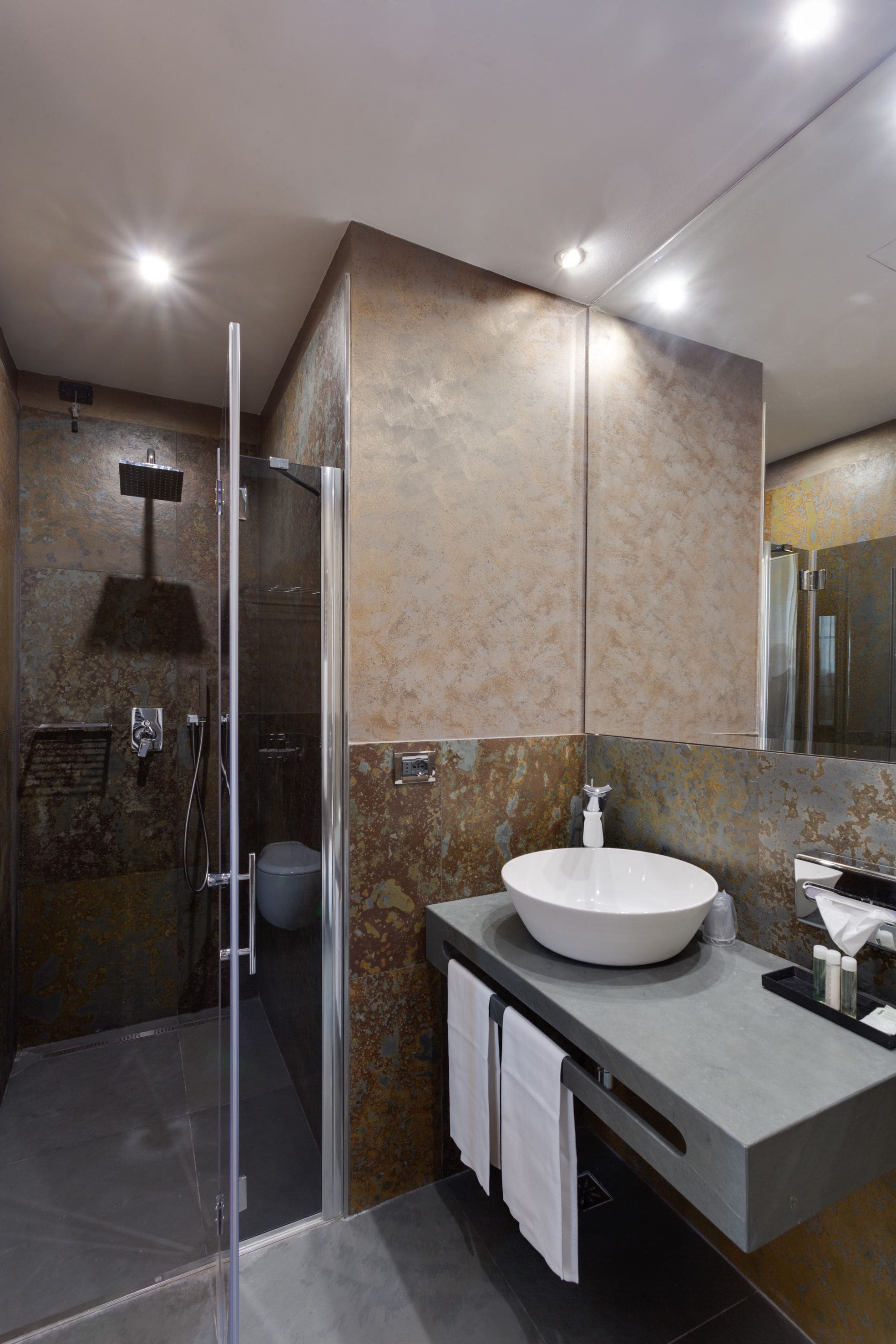Un baño moderno con ducha de vidrio, un lavamanos grande y pared revestida de mármol.