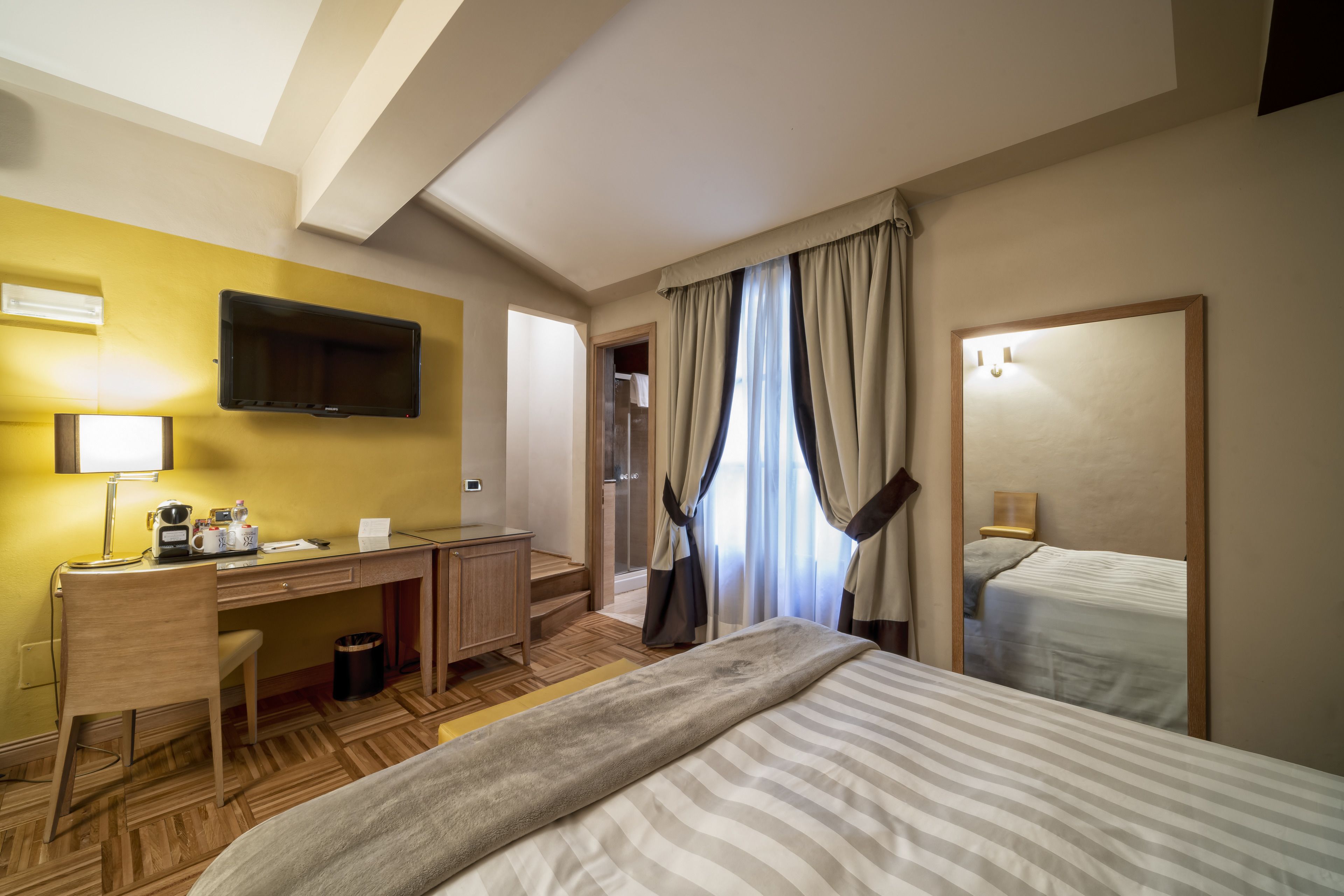 Habitación de hotel con cama, escritorio con silla, televisor y zona de ducha.