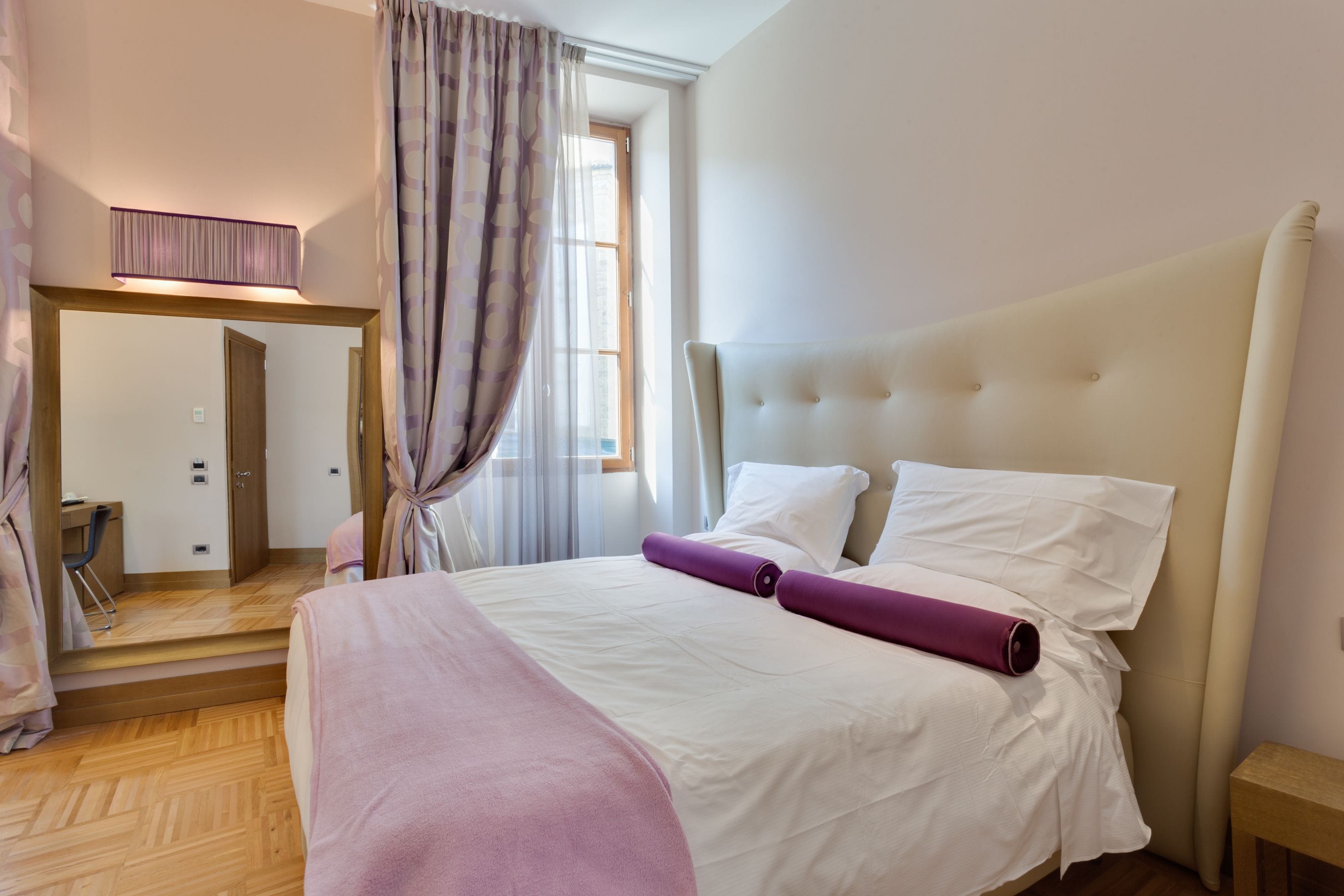 A neatly arranged bedroom with a large bed, a bedside table, and a mirror.
