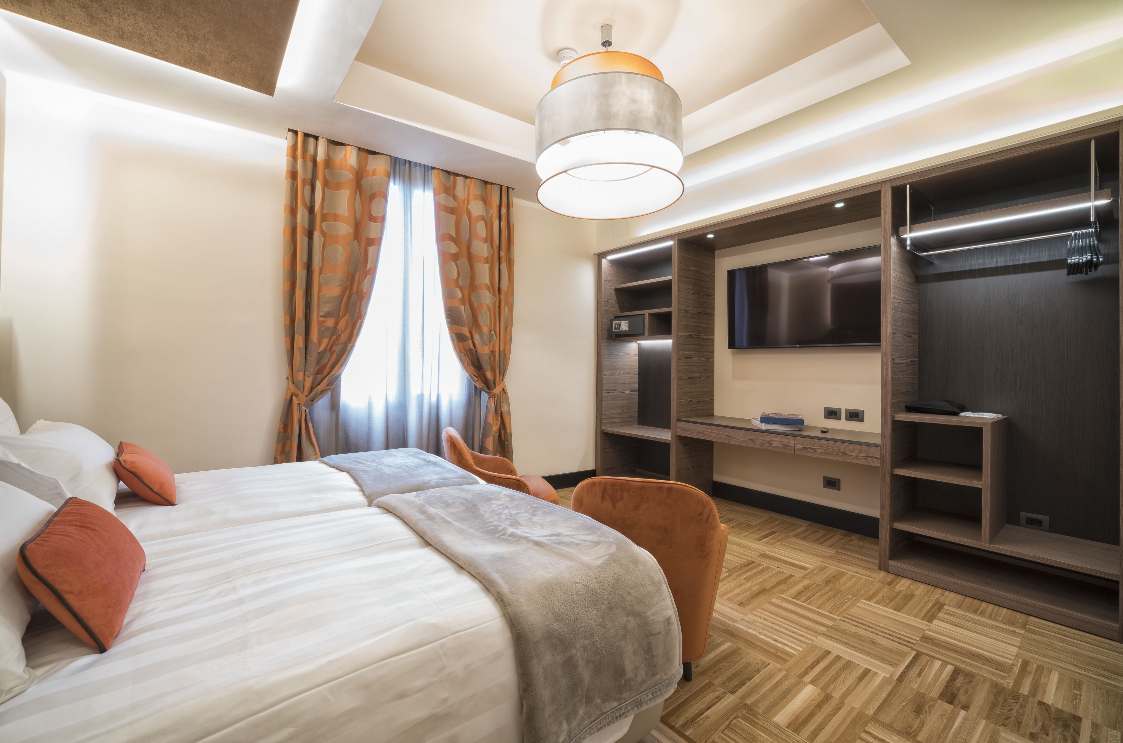 A modern hotel room with a large bed, a seating area, a TV, and built-in storage.