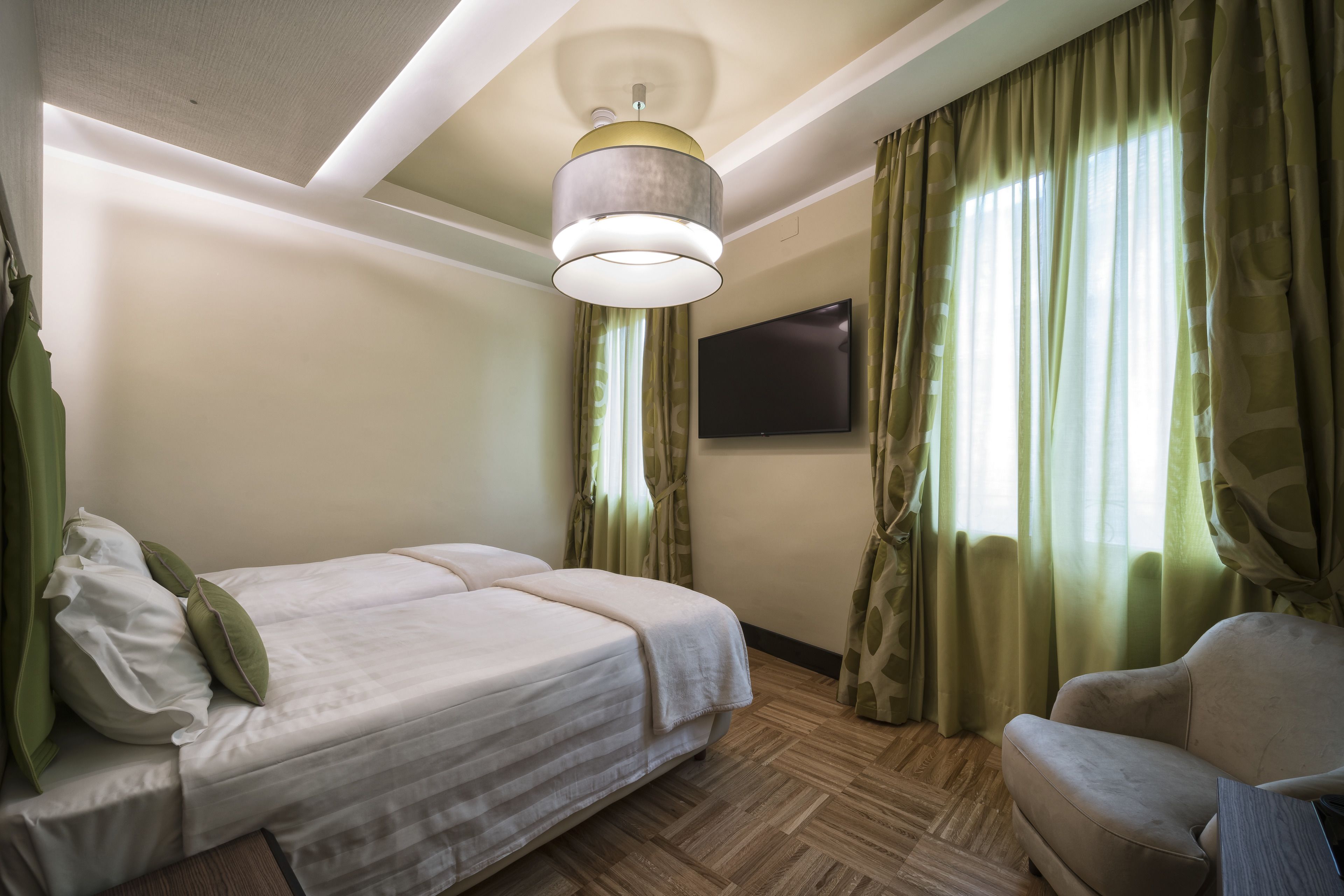 Una habitación de hotel con una cama, una silla, un televisor de pantalla plana y una lámpara en el techo.