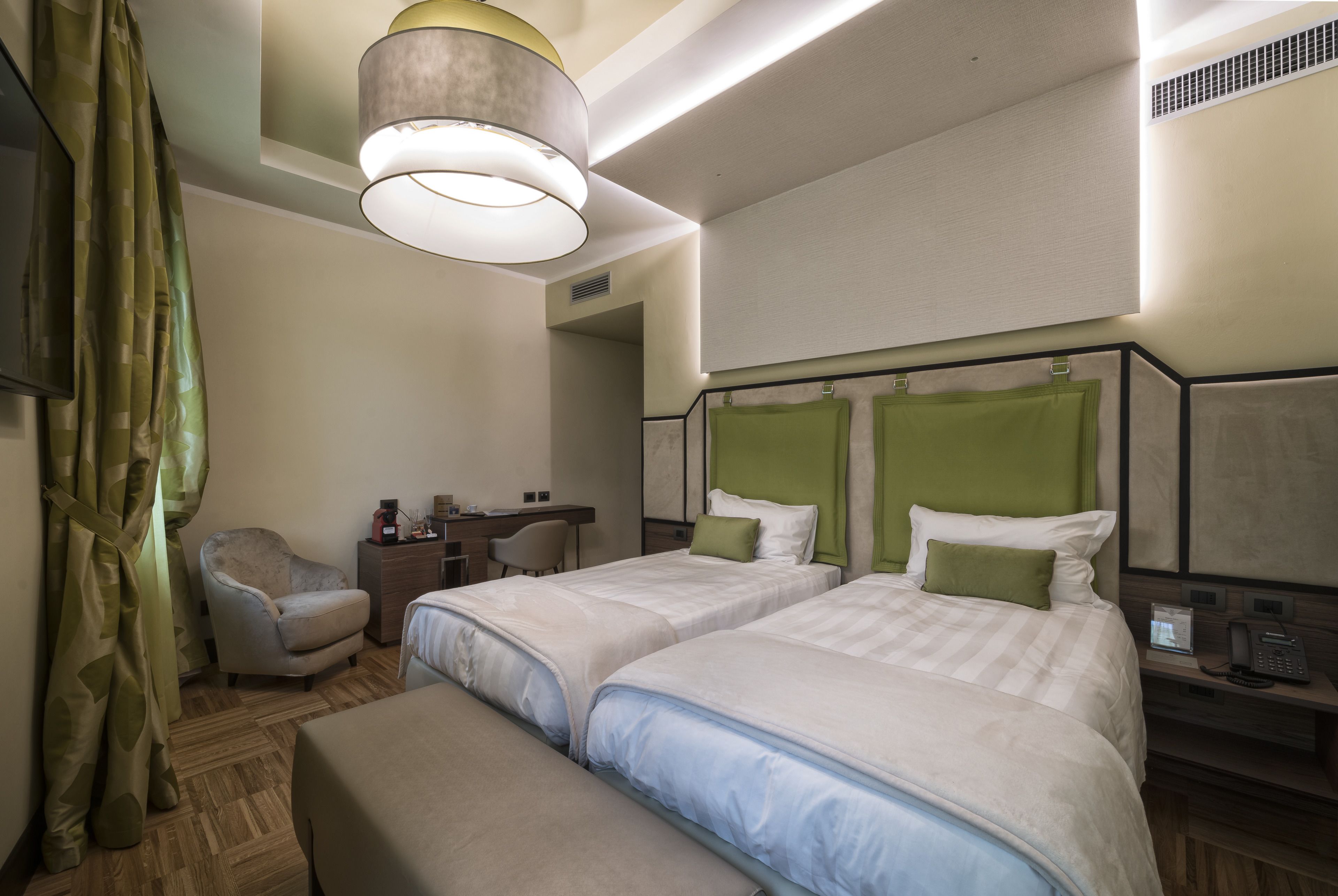 A hotel room with two beds, a desk, a chair, and a telephone.