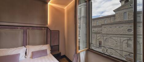 Quarto de hotel com cama, janela com vista para um edifício histórico e luminária moderna.