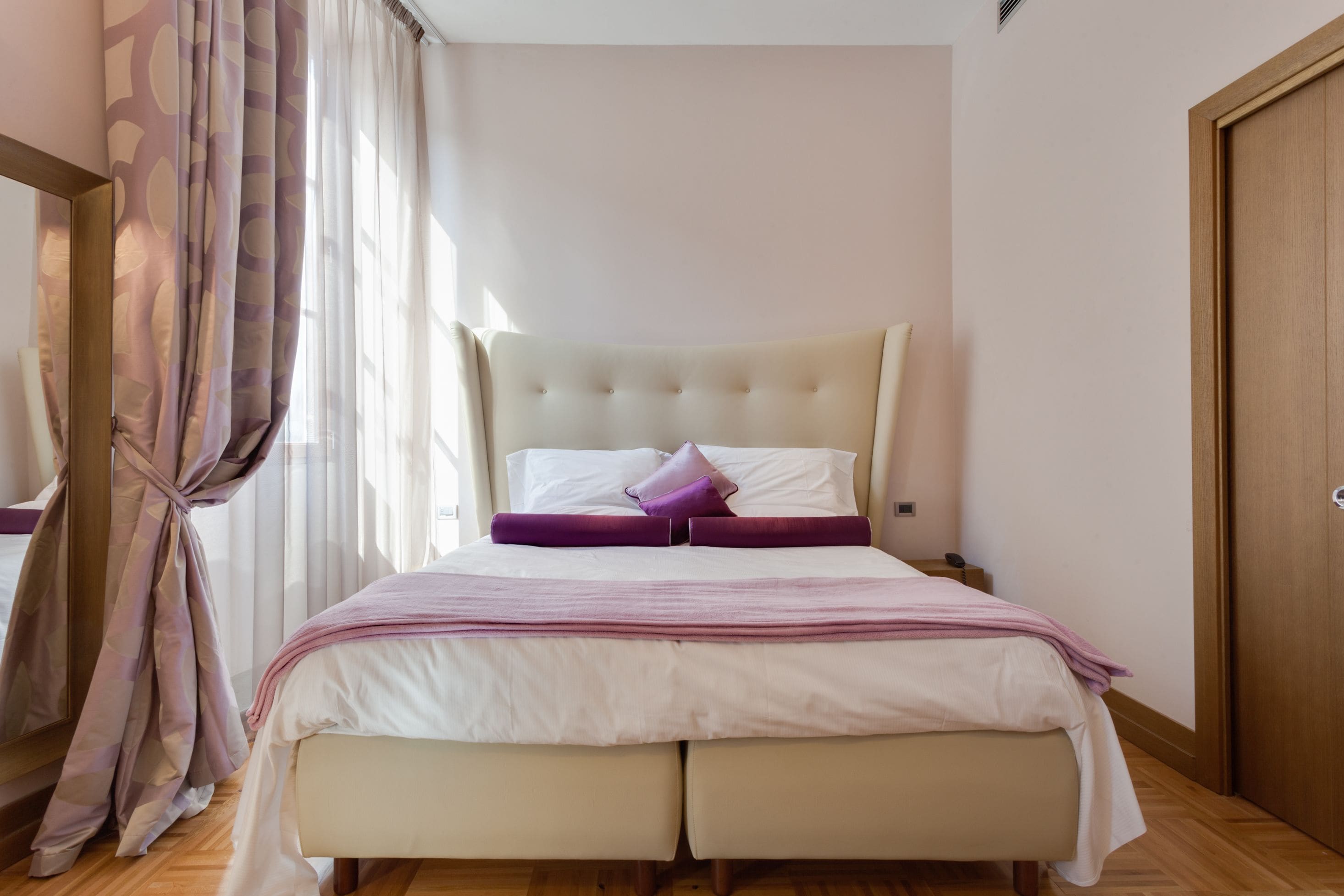 Une chambre avec un grand lit, un plancher en bois, une armoire et une fenêtre avec des rideaux.
