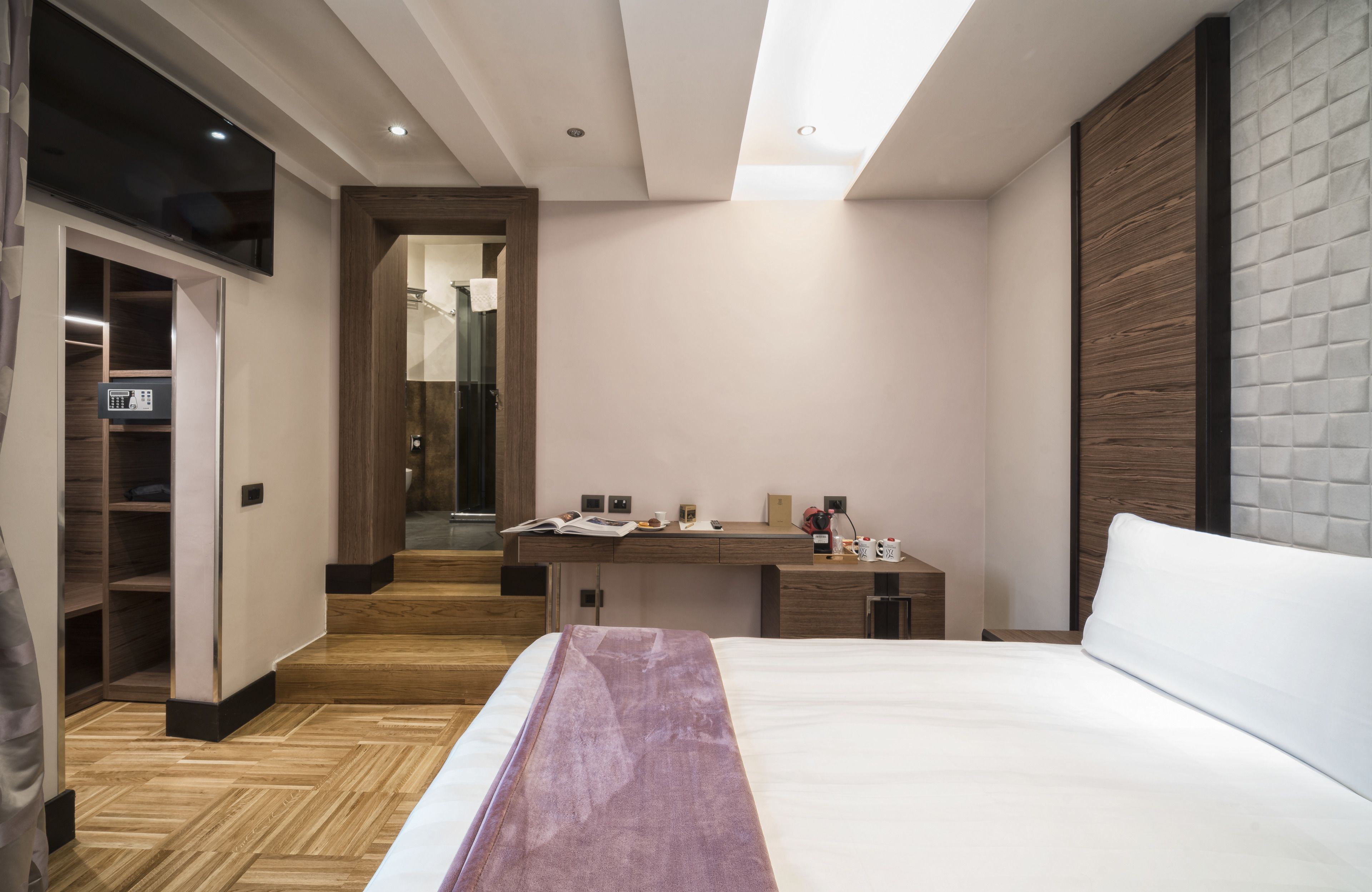 A modern bedroom with a large bed, a wooden floor, a built-in desk, and a wardrobe.
