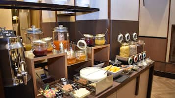A buffet with various food items and beverages, including jars of jam, honey, and cereal.