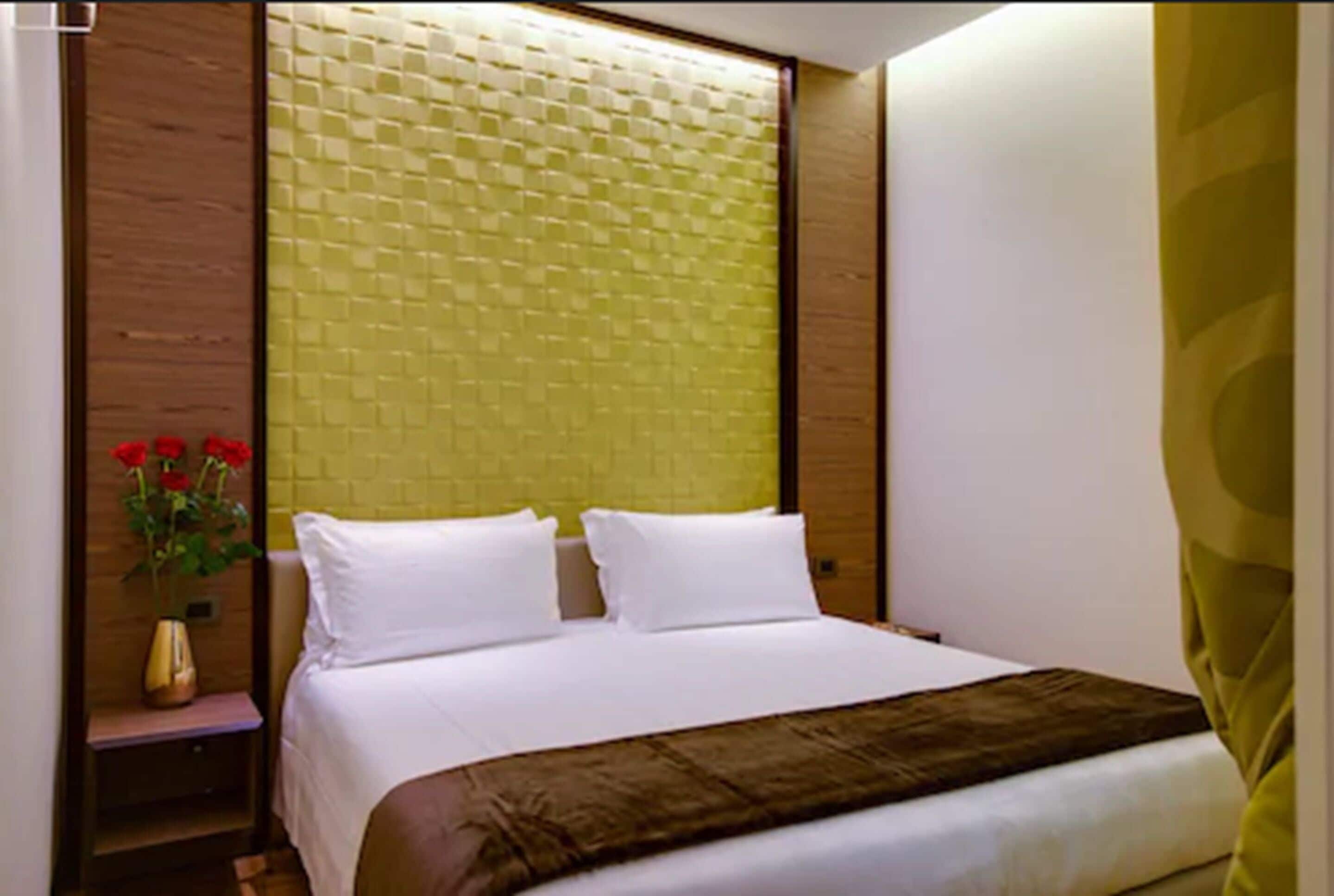 A hotel room with a large bed, a nightstand with a vase of flowers, and a green textured wall.
