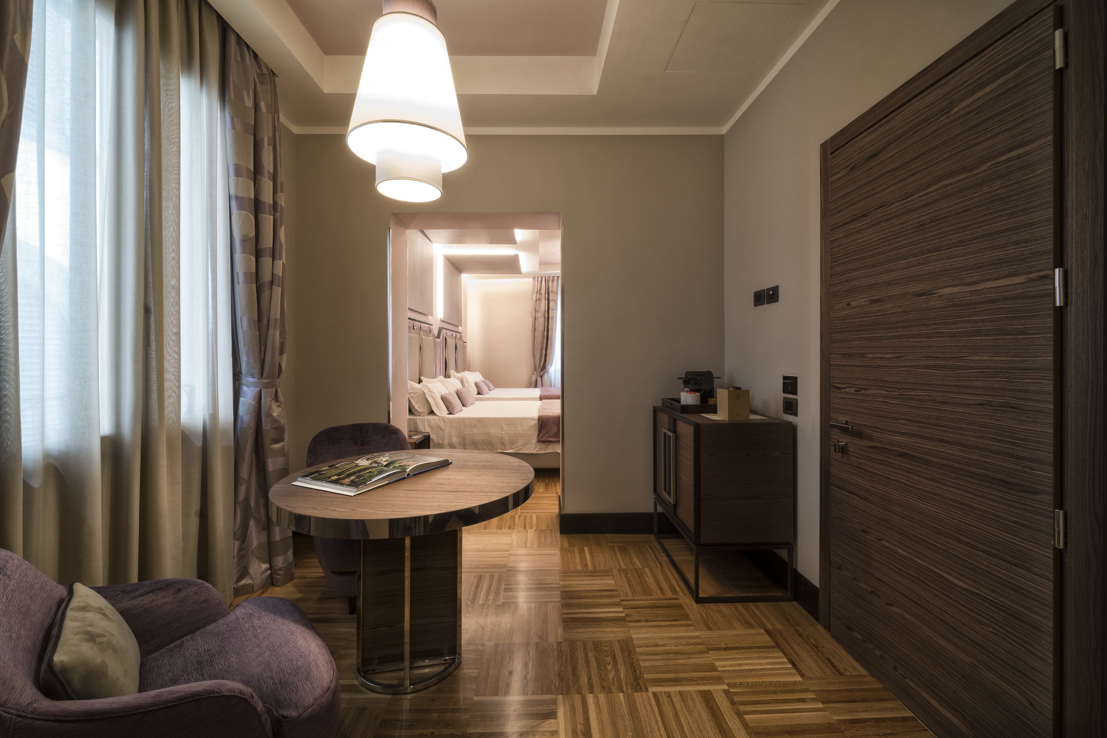 Una habitación de hotel con una mesa redonda, un sofá, un armario y un pasillo que conduce a un dormitorio.