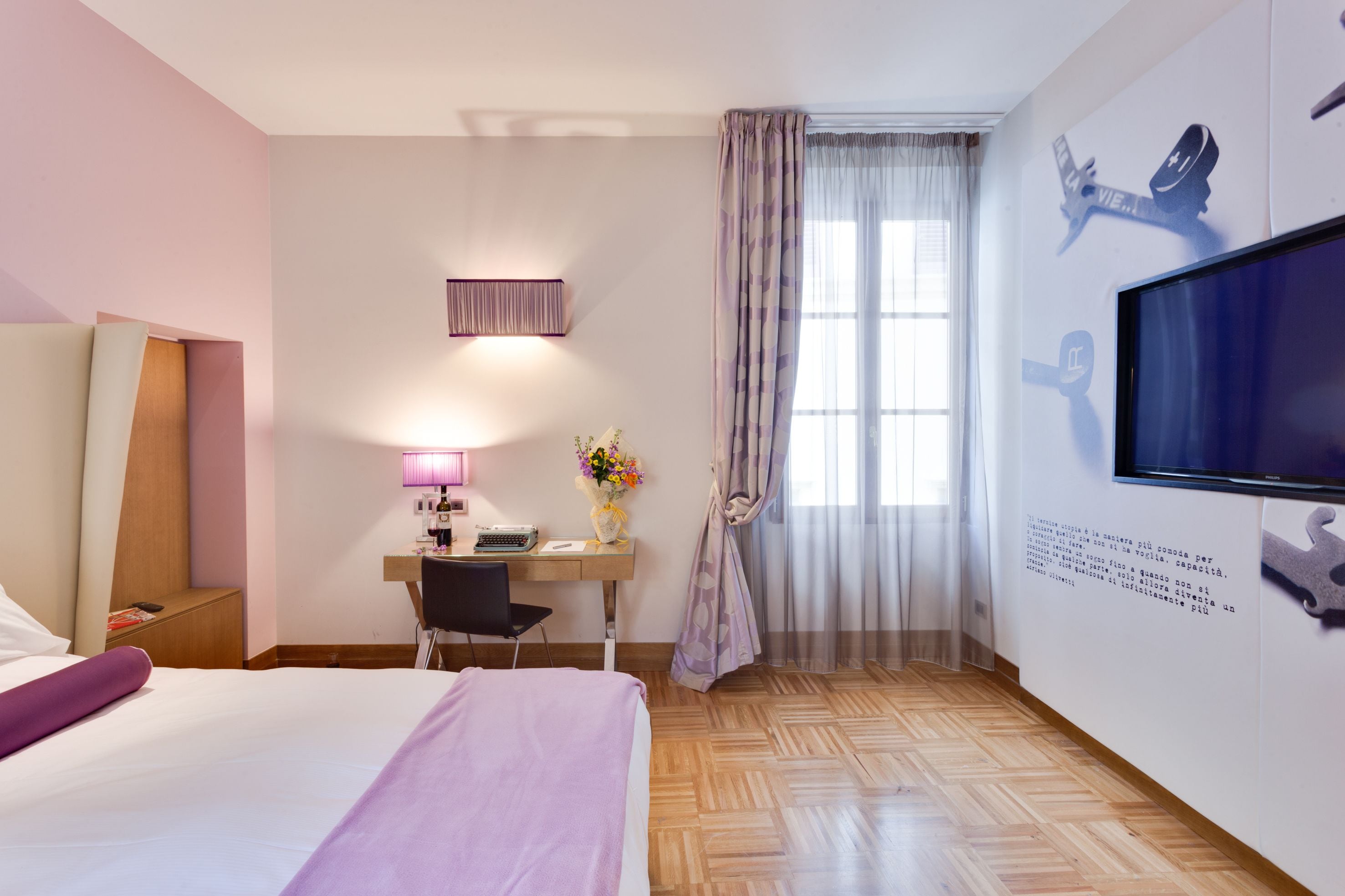 Een hotelkamer met een bed, bureau, stoel, televisie en een raam met gordijnen.