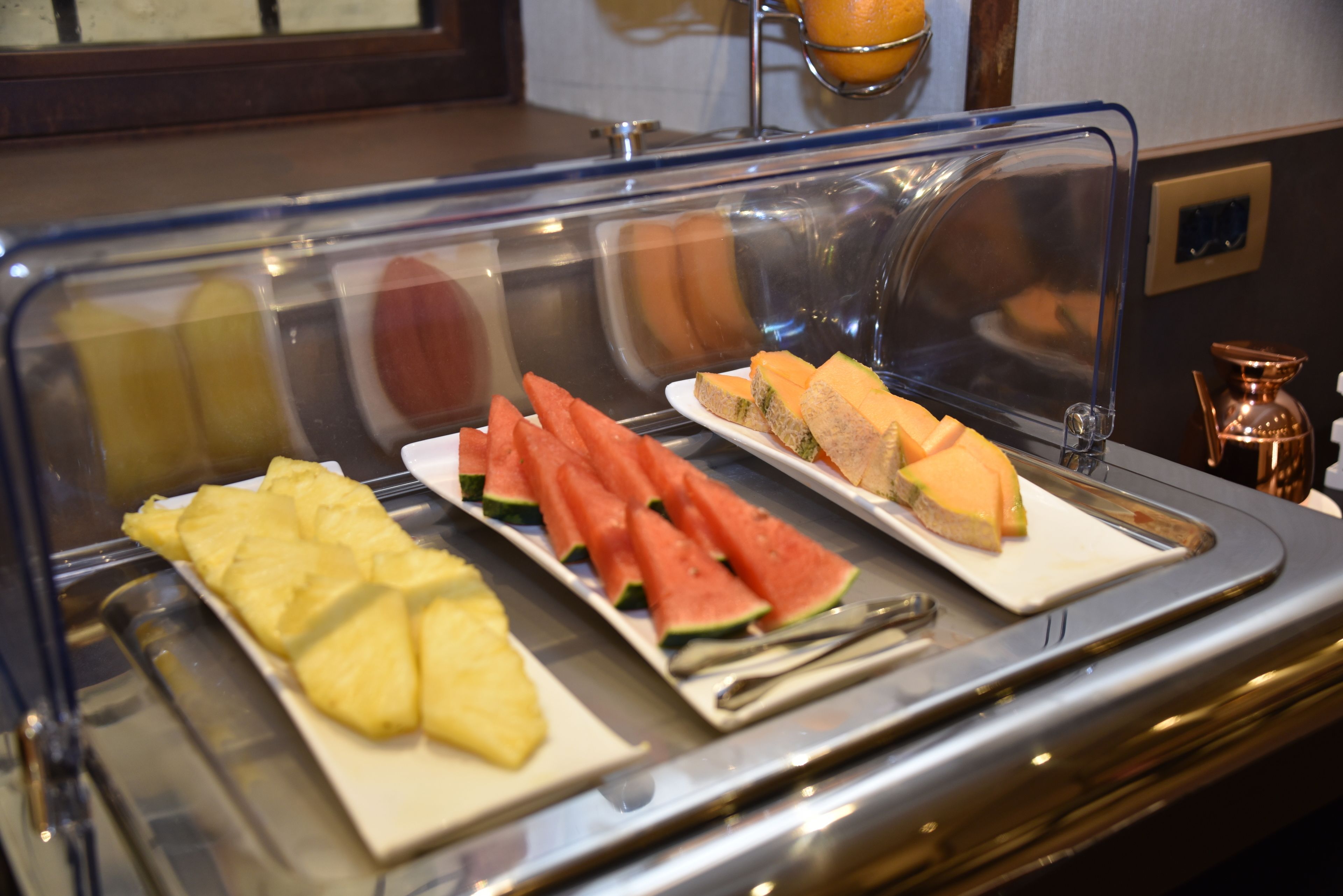 A buffet with sliced pineapple, watermelon, and sandwiches.