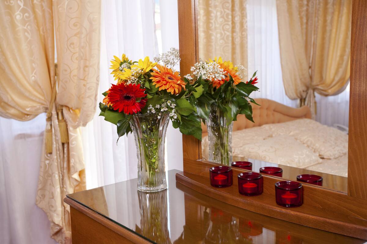 Un dormitorio con una cama, un tocador con espejo y un florero sobre el tocador.