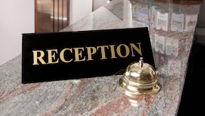 A reception area with a marble counter, a reception sign, an elevator, and a magazine rack. - Hotel Victoria (Skopje)