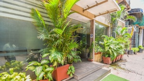 A building entrance with steps leading up to a glass door, surrounded by potted plants and a small green area. - Kings International Juhu (Mumbai)