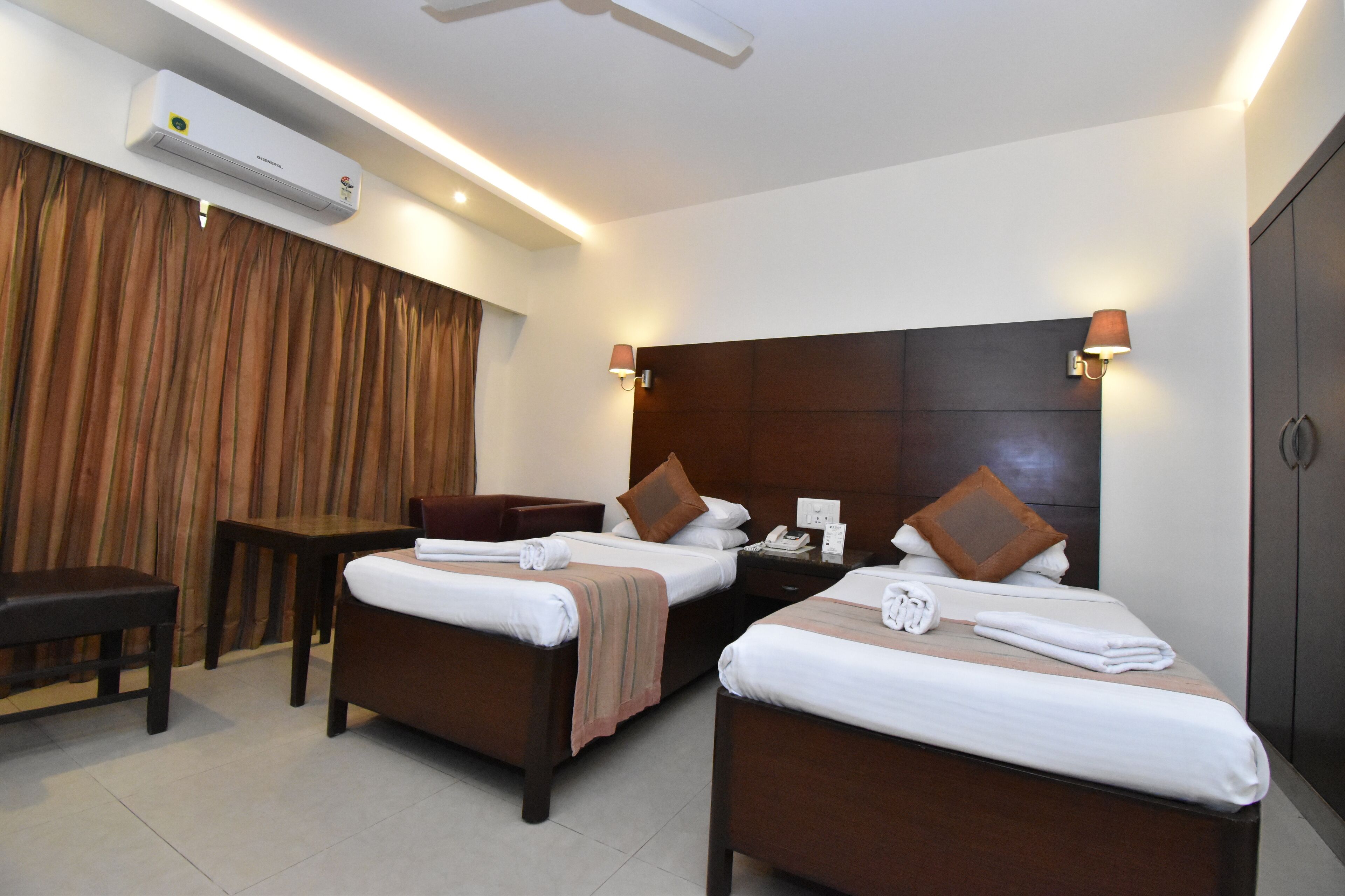 A hotel room with two beds, a desk, a chair, and an air conditioning unit.