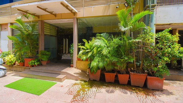 A building entrance with a covered walkway, potted plants, and a green artificial turf area. - Kings International Juhu (Mumbai)