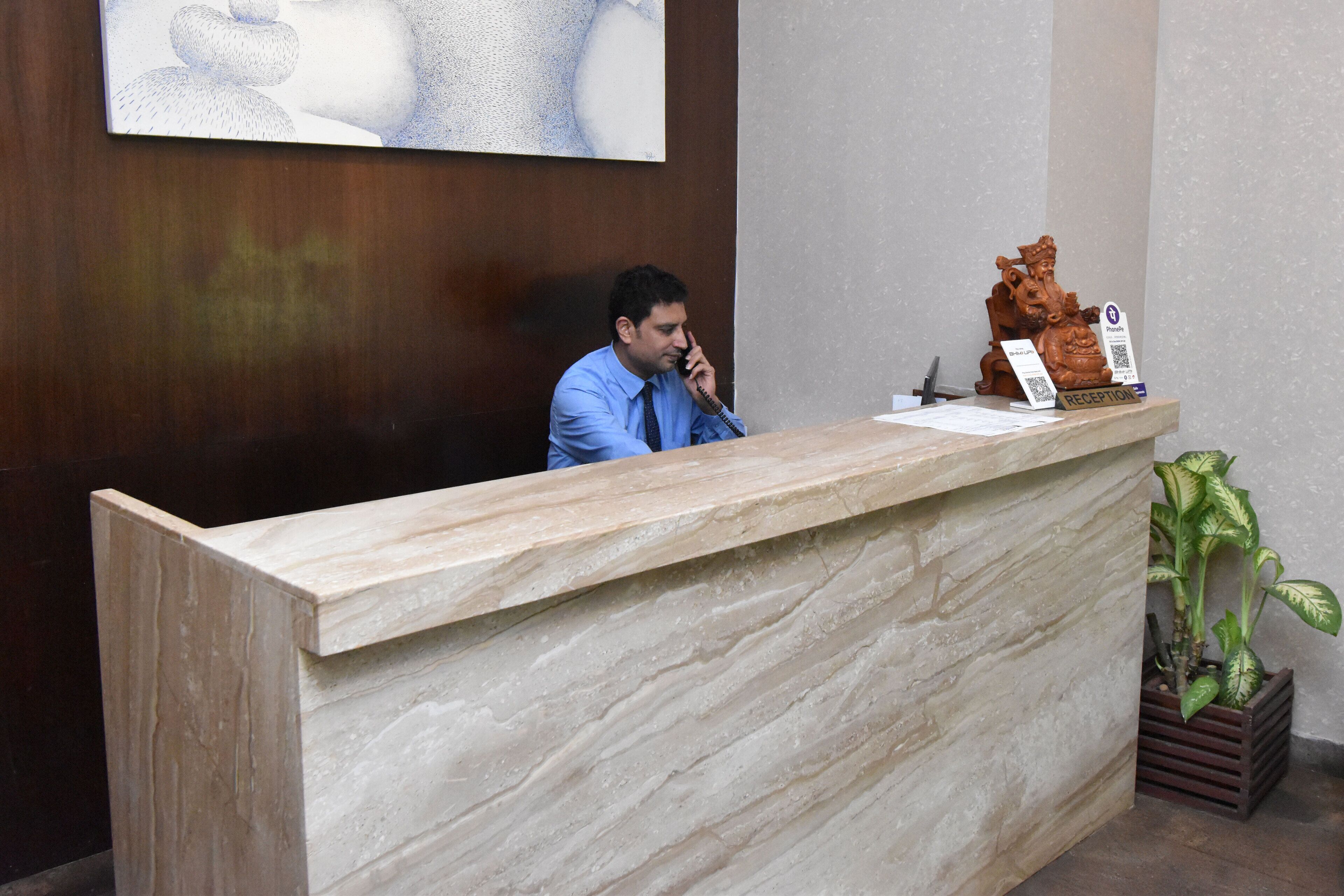 A reception desk with a marble top, a plant to the right, and a wall-mounted artwork above.