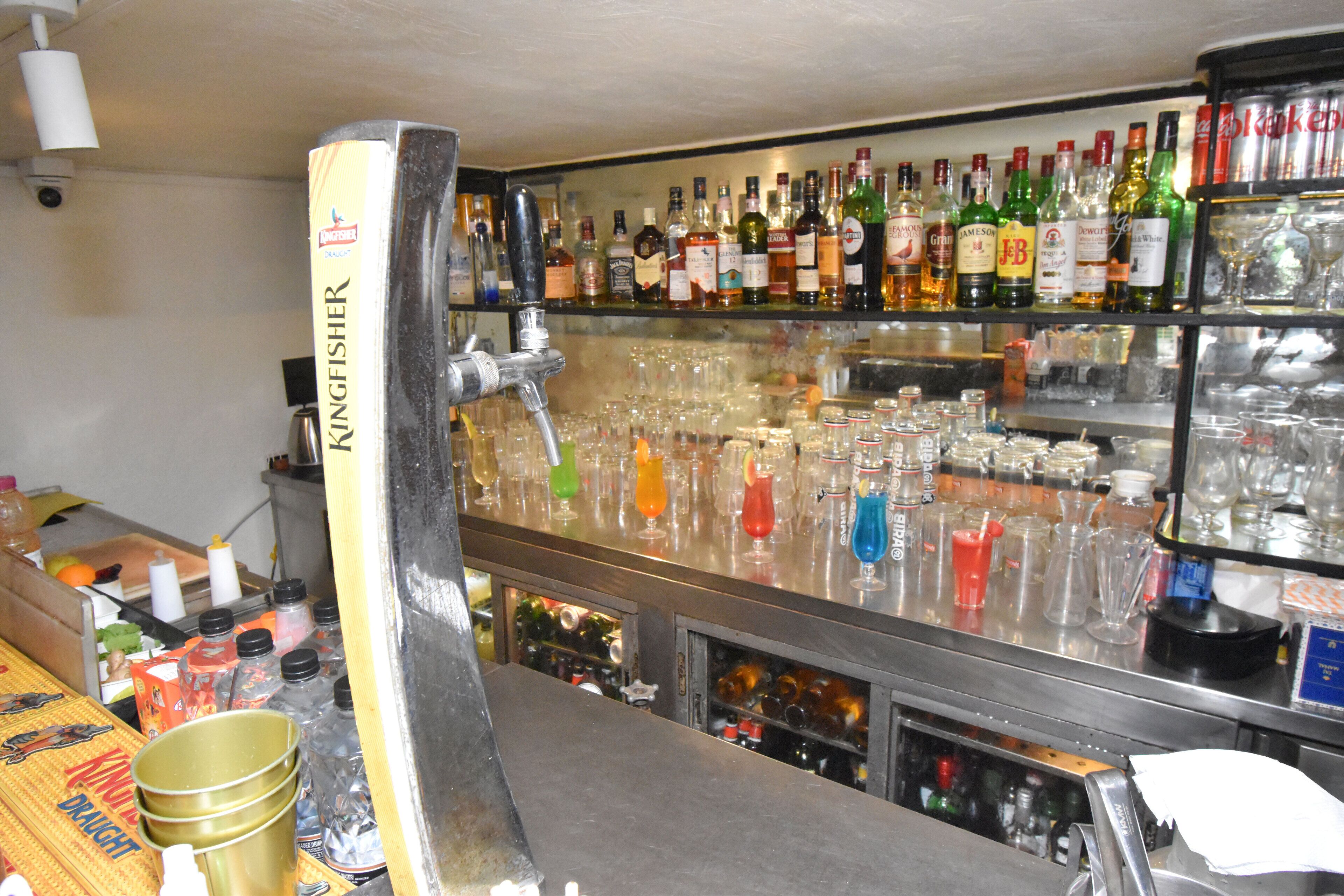 A bar area with a Kingfisher branded tap, shelves of various liquor bottles, and numerous glasses and bottles on the counter.