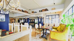A spacious room with a high ceiling, wooden flooring, a yellow sofa, a dining table, and a chandelier. - Kings International Juhu (Mumbai)