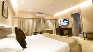 A hotel room with a large bed, a TV, a desk, and an air conditioning unit. - Kings International Juhu (Mumbai)