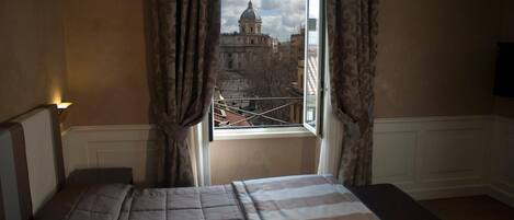A bedroom with a large bed, a window with curtains, and a view of a historic building.