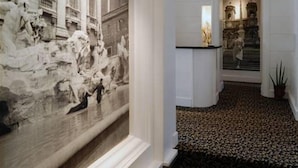 Ein Flur mit einer großen, klassisch gestalteten Wandmalerei links, einem gemusterten Teppich und einer Treppe, die zu einer zweiten Etage führt.