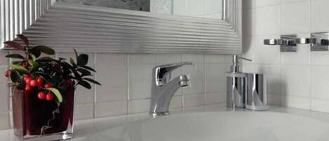 A modern bathroom with a white sink, chrome faucet, and a potted plant with red berries.