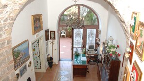 A room with a rustic stone archway, a desk with a computer, a chandelier, and various framed pictures on the walls. - L'Argine Fiorito (Atrani)