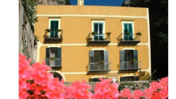 A yellow building with balconies, surrounded by pink flowers. - L'Argine Fiorito (Atrani)