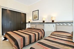 Una habitación de hotel con dos camas, un armario oscuro, un cuadro en la pared y dos lámparas de noche.