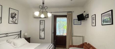 Un dormitorio con dos camas, un sofá, una lámpara en el techo, una ventana y un radiador.