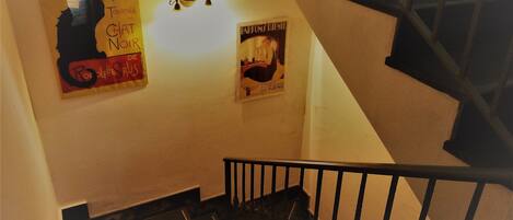 Un escalier avec une rampe noire et un mur orné de deux affiches.