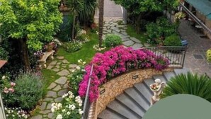 A courtyard with a stone staircase, palm trees, and flowering plants. - Albergo Pace (Pompei)