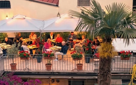 An outdoor café with tables and chairs, potted plants, and a balcony with railings.