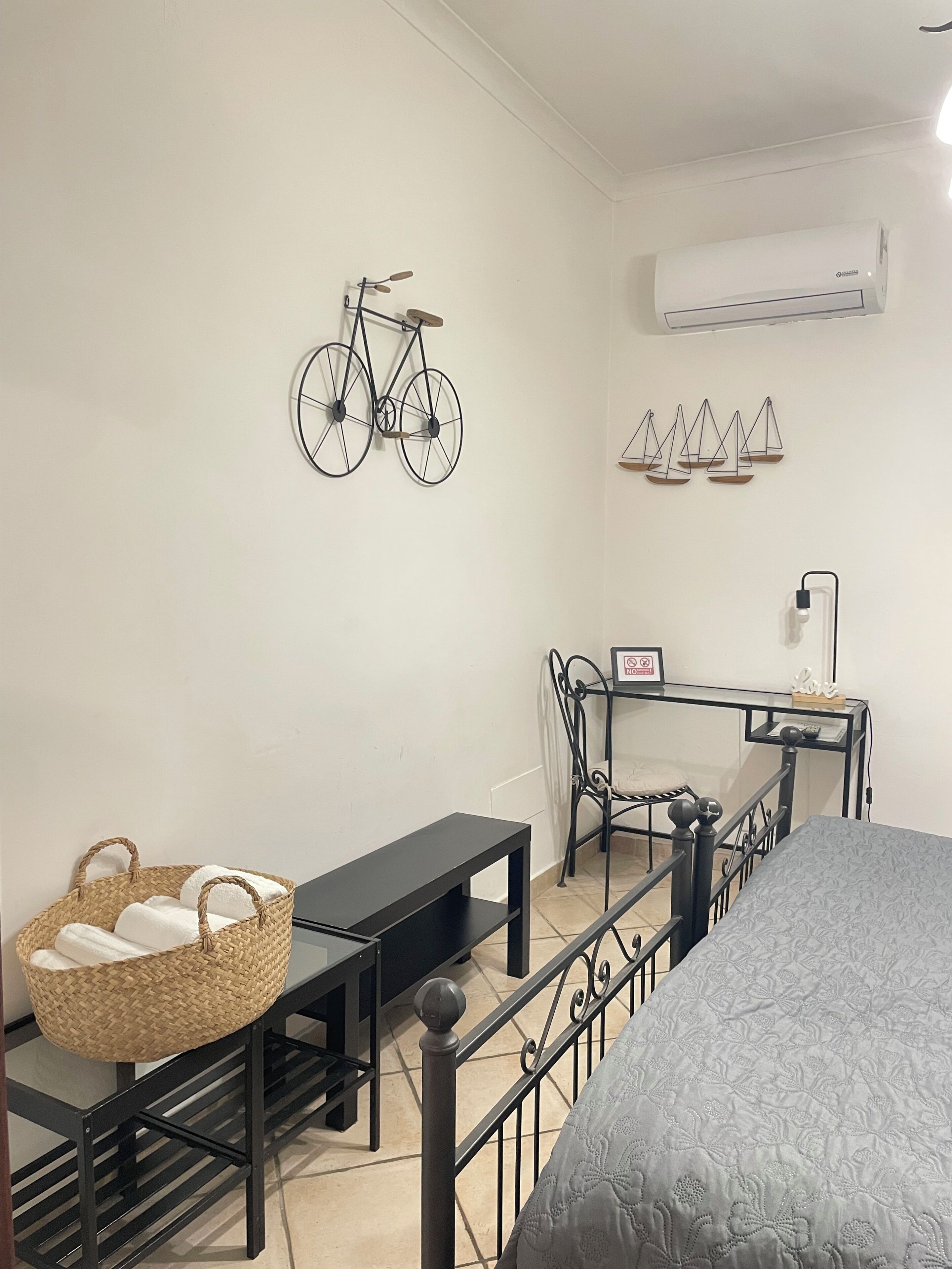 Quarto com cama, escrivaninha, cadeira, bicicleta, cesta e ar-condicionado.