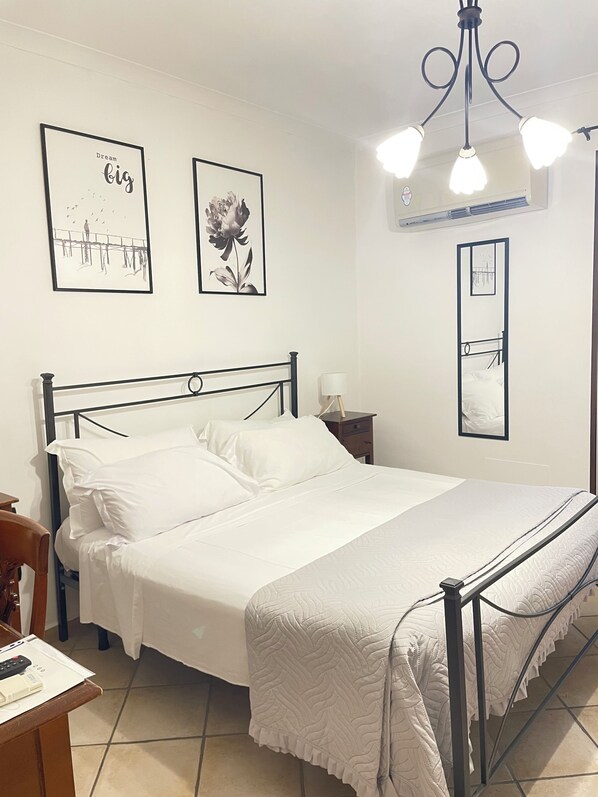 A neatly made bed with white linens, a metal headboard, and a bedside table with a lamp. There are two framed pictures on the wall, one with a bird illustration and the other with a flower. - Albergo Pace (Pompei)