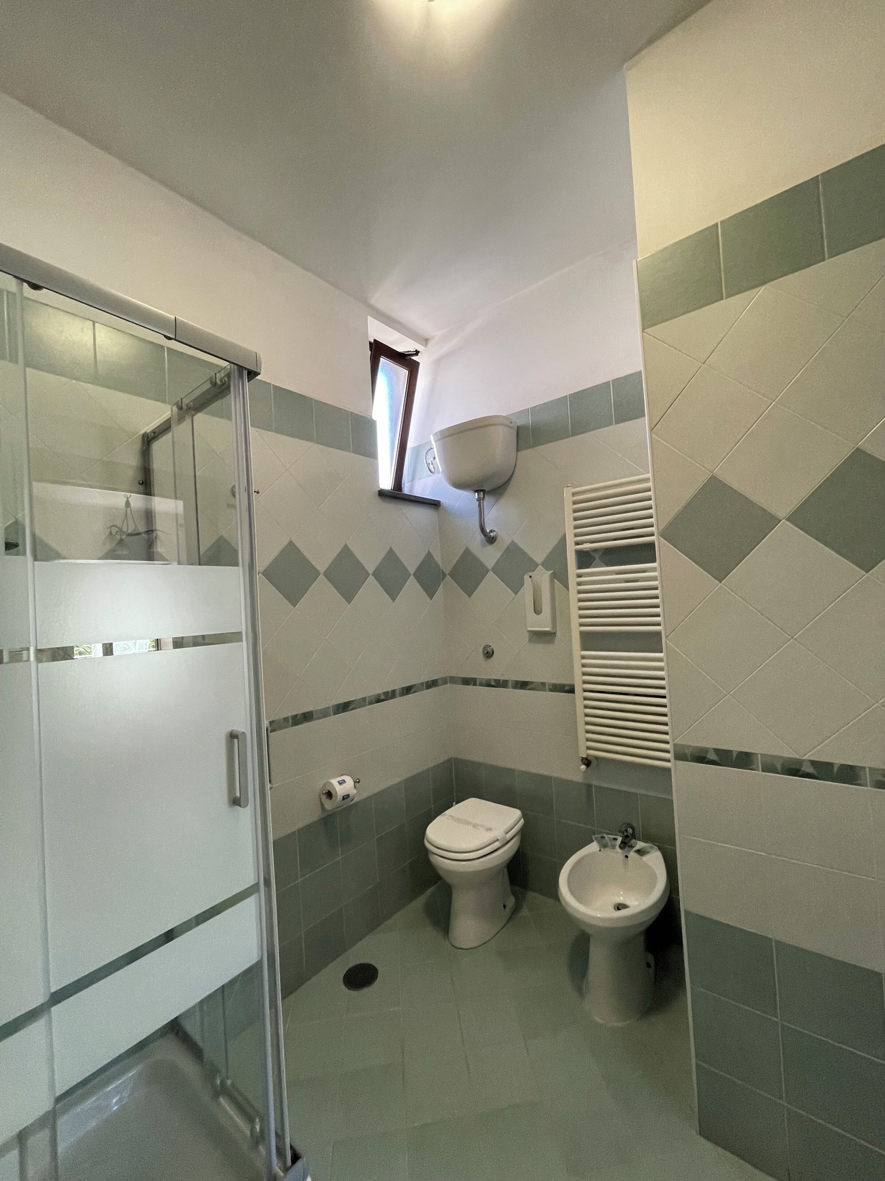 A bathroom with a glass shower enclosure, a toilet, a bidet, and a wall-mounted sink.