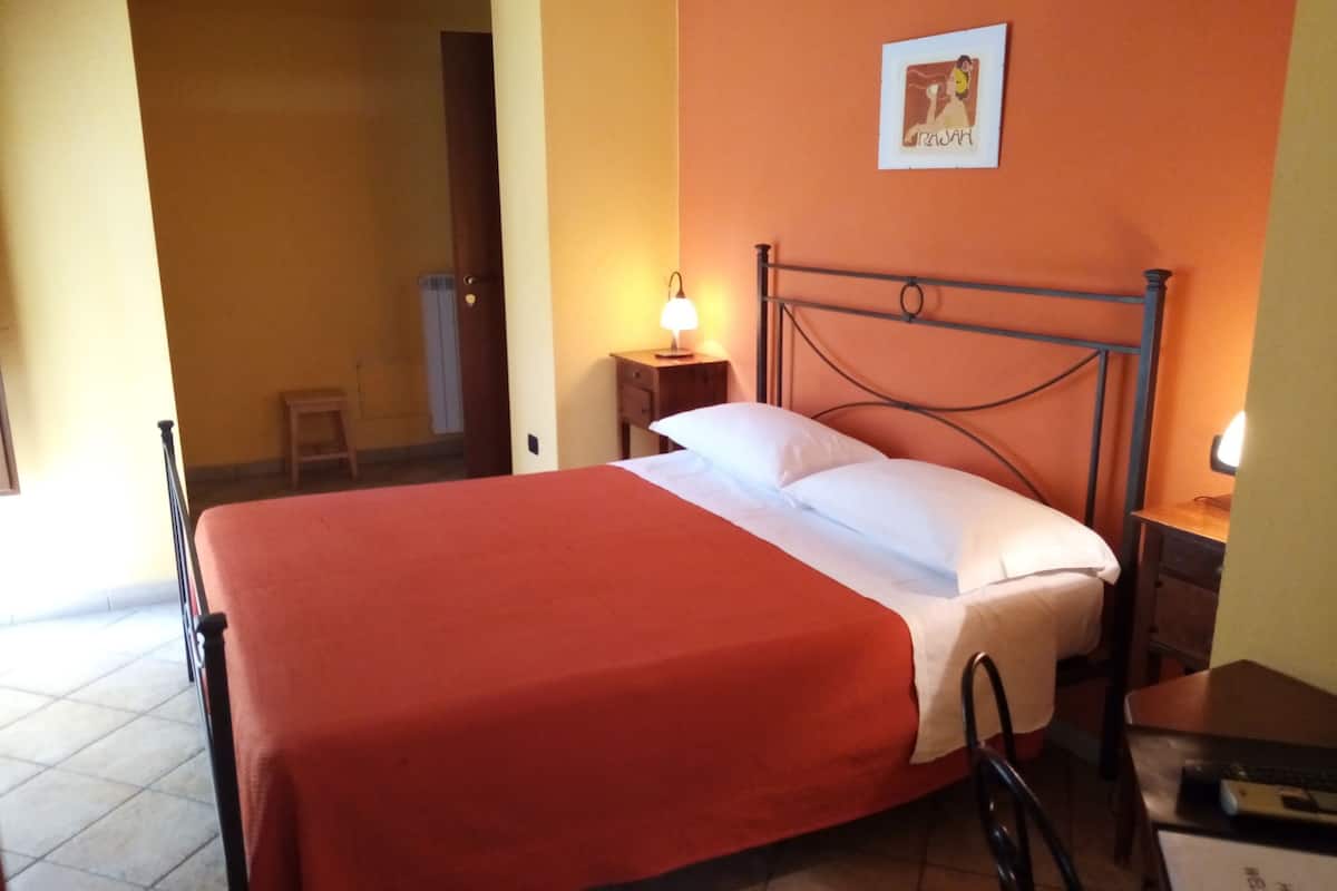 A hotel room with a bed, a nightstand, a chair, and a wall-mounted picture.