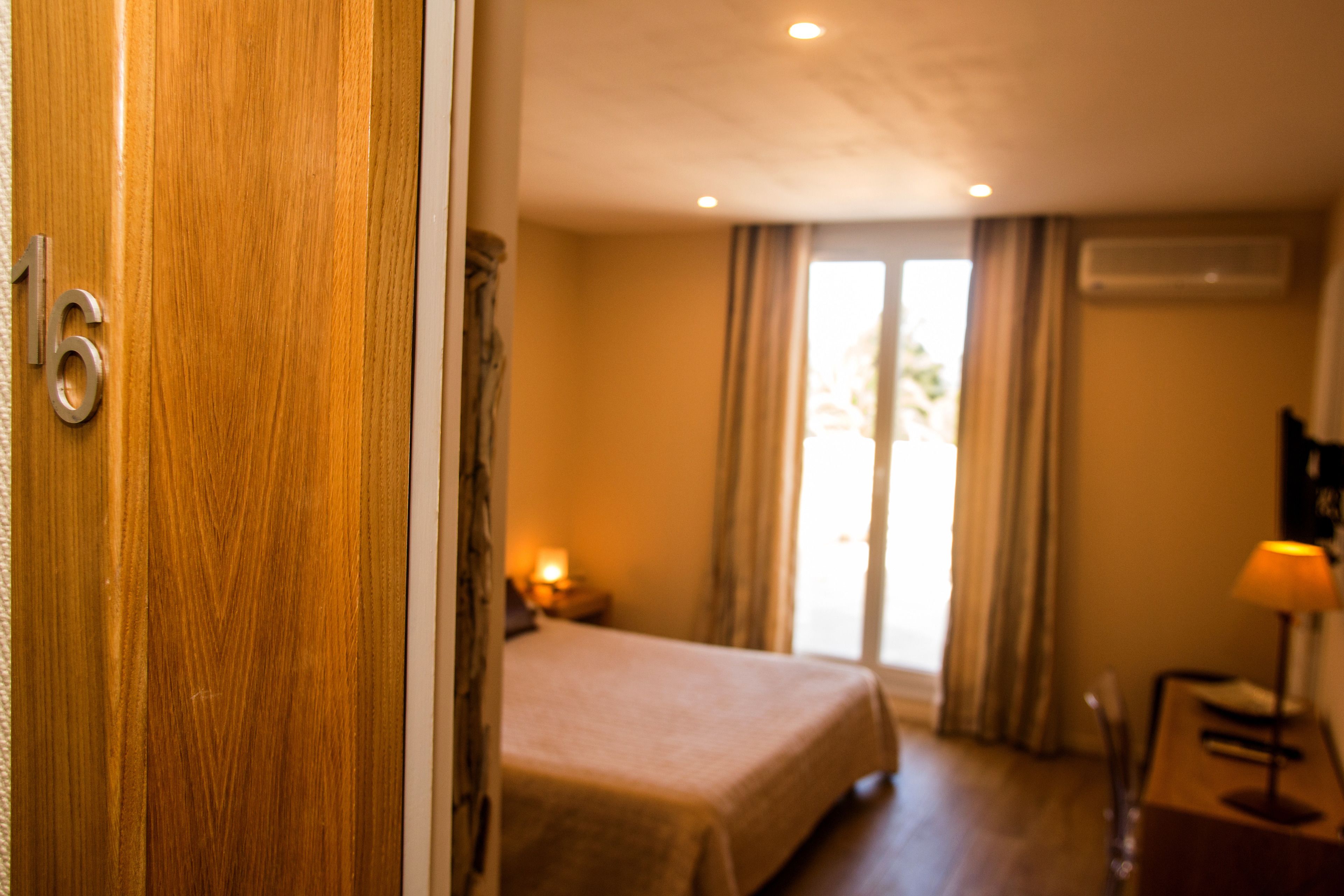 A hotel room with a bed, a desk with a lamp, and a window with curtains.