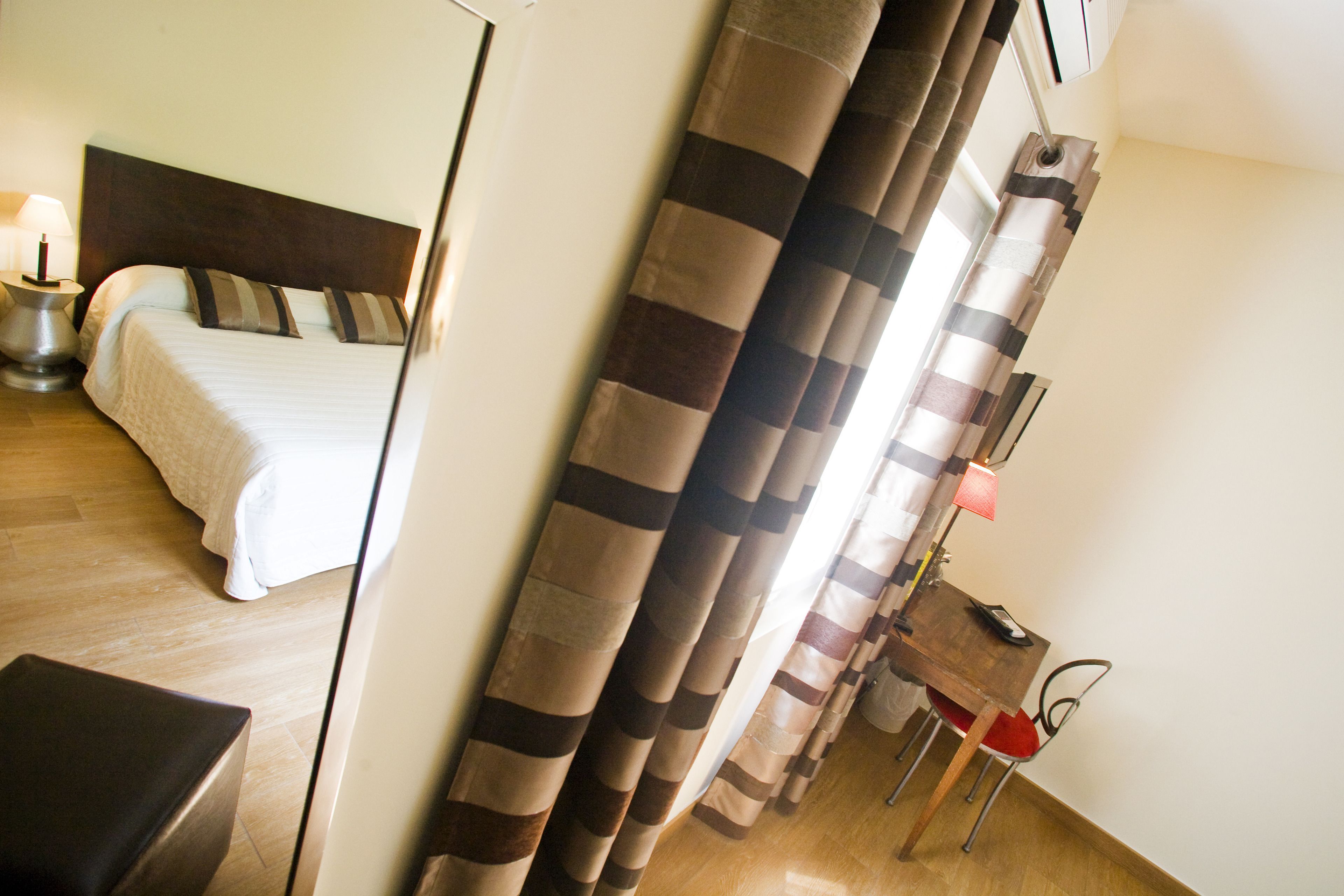 A hotel room with a bed, a desk with a chair, and curtains.
