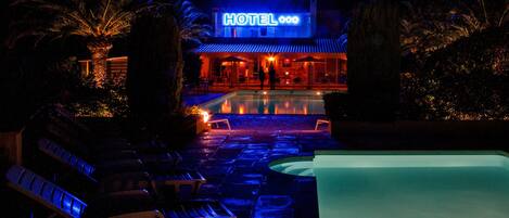 Een hotel met een zwembad, ligbedden en een bord waarop 'HOTEL' staat.