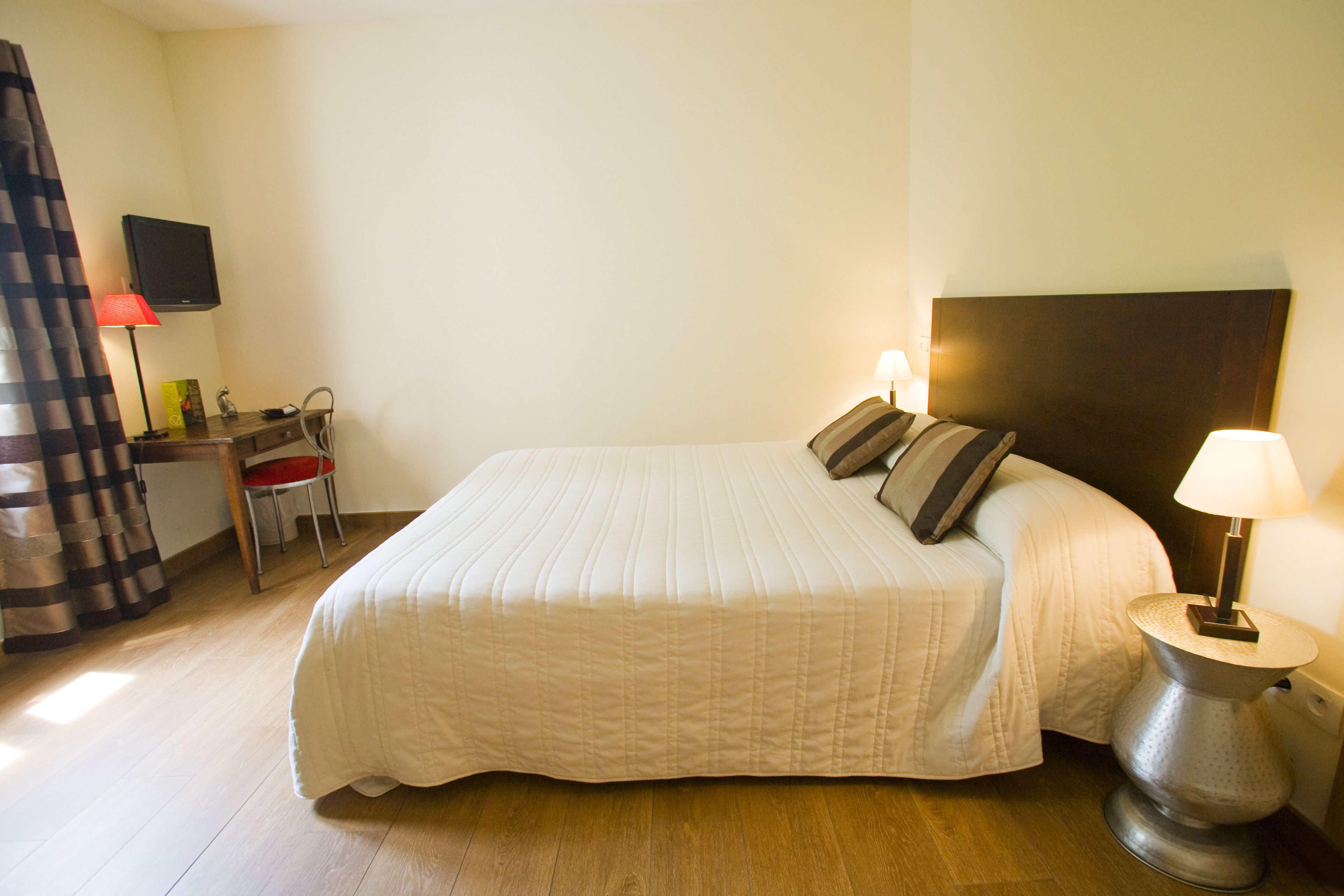 A hotel room with a bed, a desk, a chair, a TV, and a lamp.