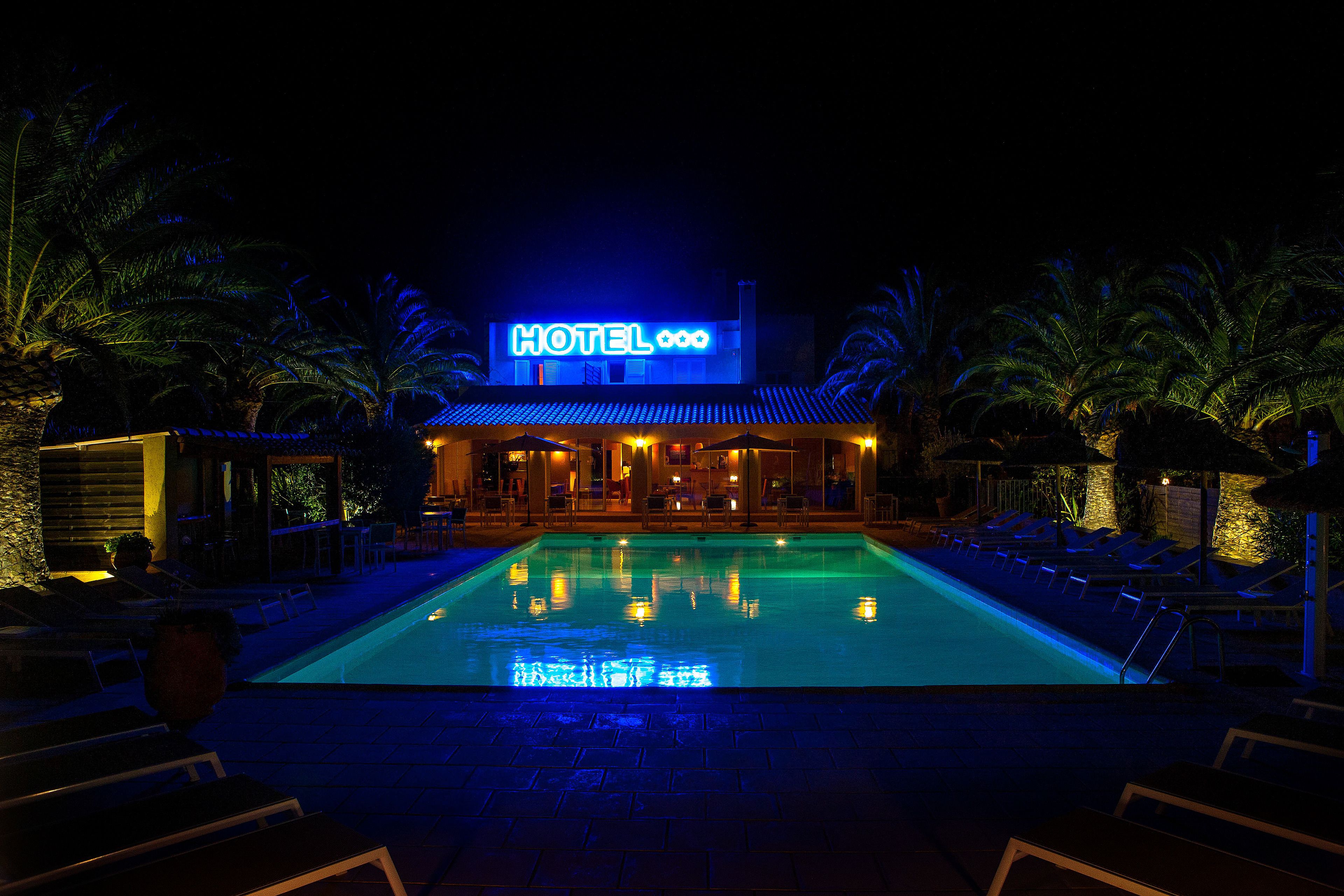 A hotel with a swimming pool, palm trees, and a neon sign.